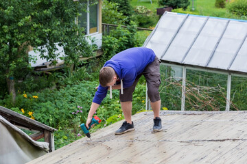 A man holds a screwdriver in his hands while standing on the roof