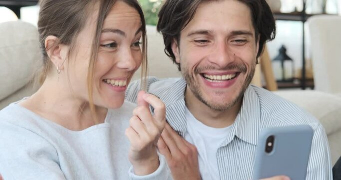Astonished couple reading good news using mobile phone at home