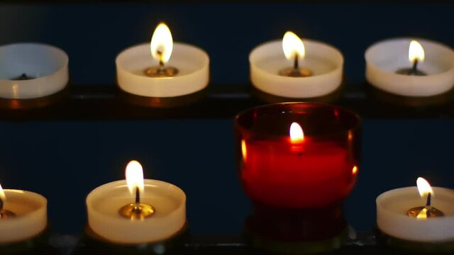 many small white and red church candles in a monastery church in UK. illuminated on black background in close up shoot
