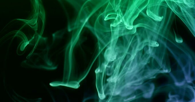 Colored green smoke swirls in different directions on a black background. Slow motion 4k DCI footage