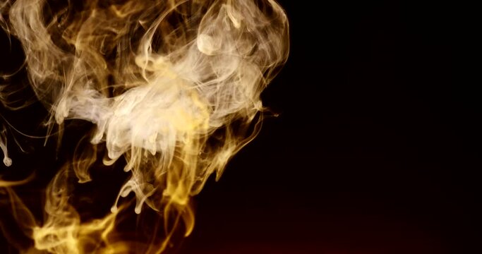 Golden colored smoke swirls up like fire and expires slowly. Isolated on black background. 4k DCI footage