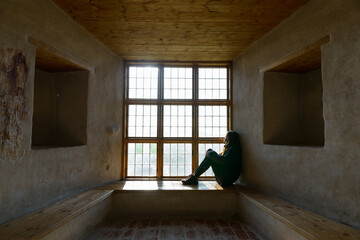 Obraz premium Young woman sitting in front of closed wooden window with sunlight streaming in