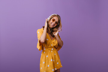 Glamorous pretty girl posing in headphones. Indoor portrait of sensual blonde lady with tanned skin wears orange dress.