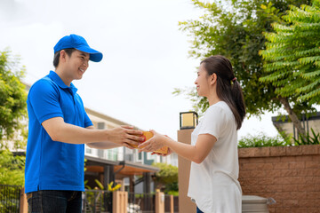 Fototapeta premium Asian delivery young man in blue uniform smile and holding a cardboard boxes in front house and Asian woman accepting a delivery of boxes from deliveryman. Advertising, Transportation Concept.