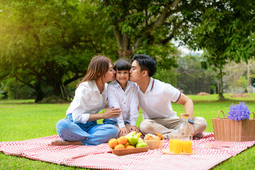 Asian teen family happy holiday picnic moment in the park with father, mother kissing daughter...