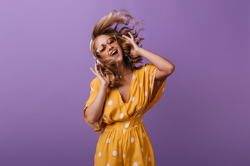 Pretty laughing lady expressing emotions during photoshoot. Indoor photo of graceful blonde girl in yellow dress.