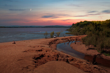 Playa con atardecer y luna de fondo, arena rojiza 