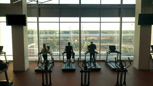 Three sporty guys, two men and woman running on treadmills in a gym. Shooting from a high point, flying out. Empty gym.