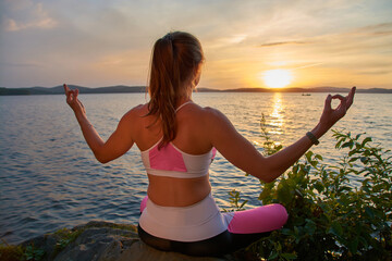 A young woman with long hair practicing yoga by the sea at sunset. The concept of harmony, meditation and travel. Healthy lifestyle