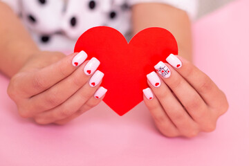 Close up view of beautiful female hands with creative manicure nails, white gel polish, hearts design, on pink background

