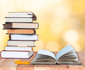 stack of books with open book and maple leaf on the wood table