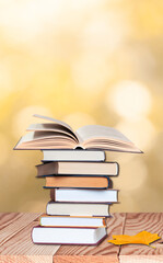 stack of books with open book on the wood table top with maple leaves on the autumn background