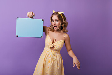 Good-looking slim lady with tanned skin posing with valise. Indoor photo of glad fair-haired girl with blue suitcase.