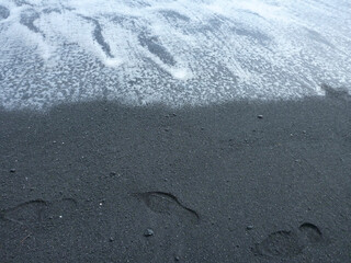 Foot prints on Punalu'u black sand beach on the Big Island of Hawaii as the surf rolls in