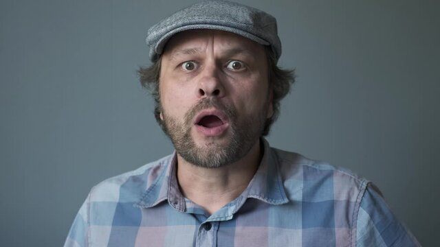a curious funny surprised Middle-aged  man who is looking at the camera. Humorous portrait of a man with no cut hair in cap.