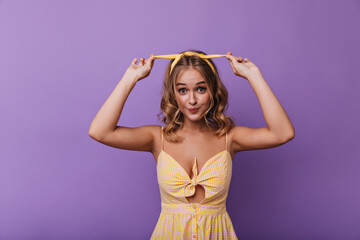 Cheerful woman in yellow dress fooling around in studio. Appealing girl with tanned skin touching her ribbon.