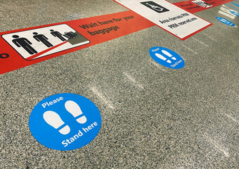 Stickers on the floor near the baggage claim belt at the airport that warn of keeping social...