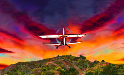 Vintage biplane flying through blazing sunset skies landscape.
