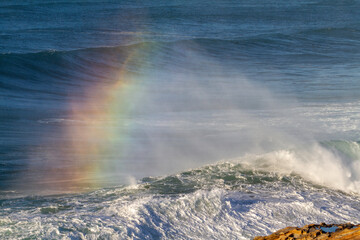 breaking wave at beach with rainbow in it