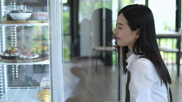 Coffee shop concept. An Asian woman is putting the cake in the freezer. 4k Resolution.
