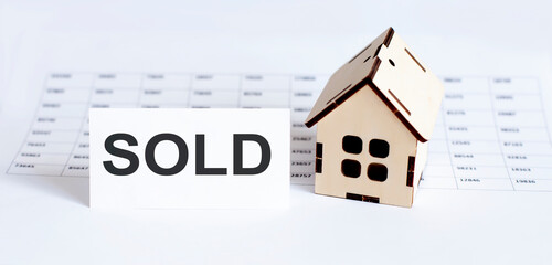 Closeup of house wooden model with blank for text SOLD on chart background.