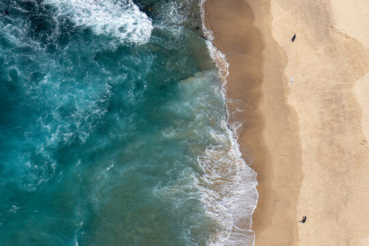 Aerial View of beach in winter with silhouettes of two people sitting on it, enjoying the peace and calmness of being alone
