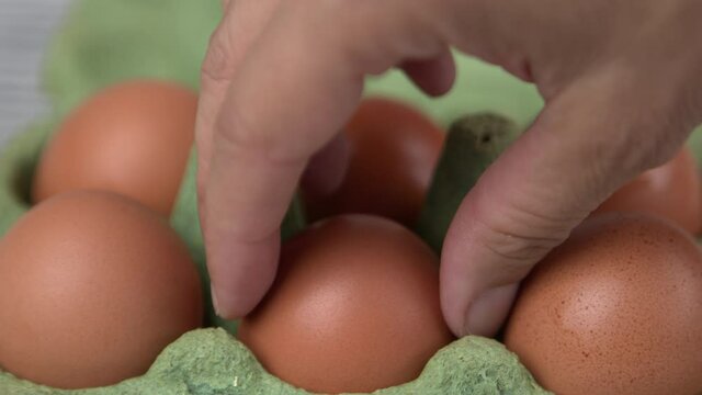 Woman's hand taking an organic egg from a green recyclable paperboard eggs carton to cook something or prepare breakfast in the kitchen. Slow-motion.