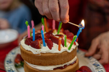 lighting candles on birthday cake with strawberries and cream on top of cake

