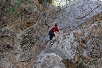 Girl wearing a red plaid shirt and jean skit climbing a rock formation at Greenough Park Missoula Montana