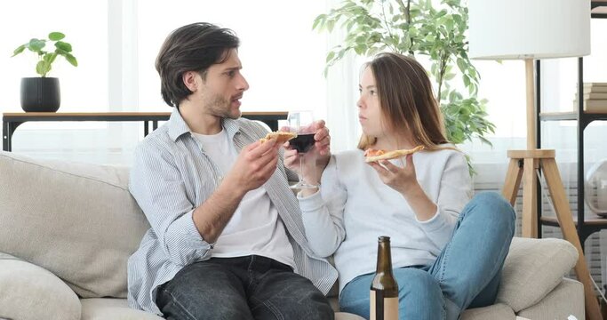 Couple eating pizza and drinking red wine sitting on sofa at home