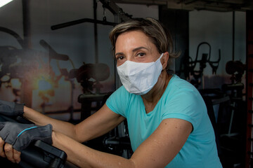 Fit Lady Working out on a Stationary Bike Wearing a Protective Mask 