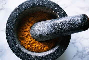 Vivid orange from Turmeric spice in dark stone mortar and pestle