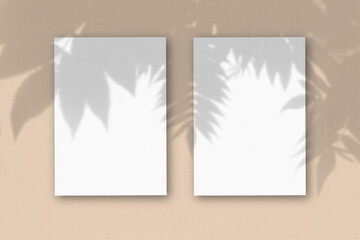 2 vertical sheets of textured white paper on peach table background. Mockup overlay with the plant shadows. Natural light casts shadows from an exotic plant. Horizontal orientation