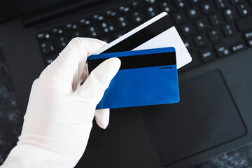 hand holding payment cards with disposable gloves on top of laptop keyboard in order not to touch...