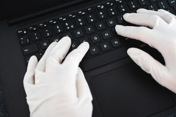 hands typing on shared computer keyboard at work wearing disposable gloves to avoid contact with potentially infected surfaces