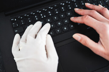 hand typing on shared computer keyboard at work wearing disposable glove to avoid contact with potentially infected surfaces and other hand without glove