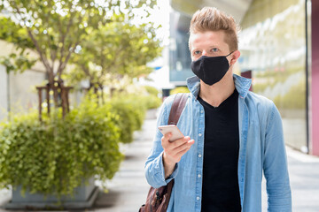 Fototapeta premium Portrait of man with mask thinking while using phone in the city outdoors