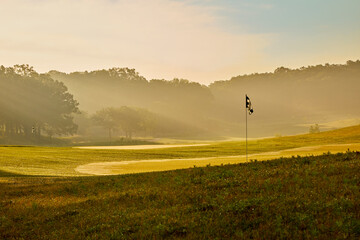Sunrise image over a beautiful golf course on a summer morning with fog and back lite sun rays