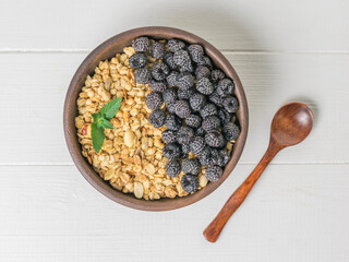 Top view of a clay bowl with granola and black raspberries on a white table.