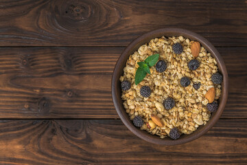 Top view of a clay bowl with granola, berries and almonds on a rustic table.