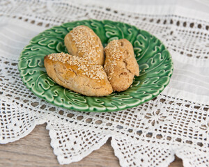 Sticks of chorek (Armenian sweet bread) with sesame seeds on green ceramic dish sitting on homemade lace table rummer. 