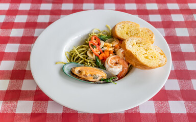 Spaghetti al pesto with chili shrimp and mussels on white plate
