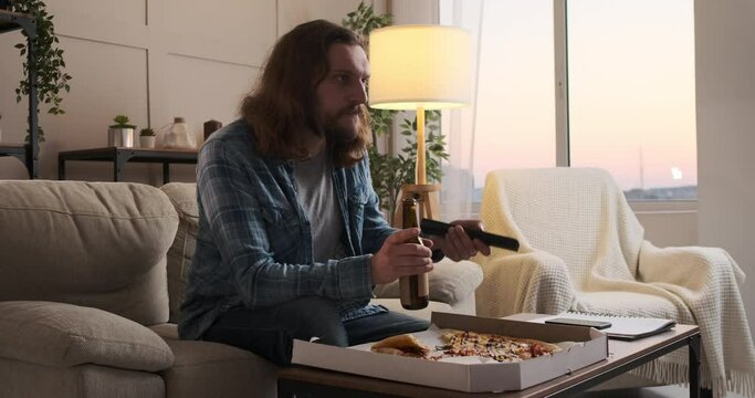 Man eating pizza and drinking beer while watching tv at home