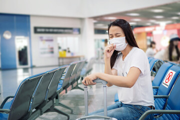 Asian tourist feeling sick, coughing ,wearing mask and sit on chair with social distancing to prevent pandemic during travel at airport terminal. new normal after coronavirus, covid-19 virus epidemic