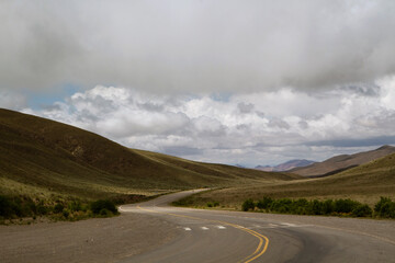 Rural scenery. Countryside road across the yellow meadow in autumn. View of the asphalt highway in the golden valley and mountains.