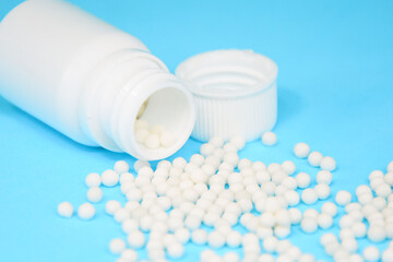 Homeopathic pills, globules and white plastic bottle on blue background close up. Alternative Homeopathy medicine herbs, healtcare and pills concept. 