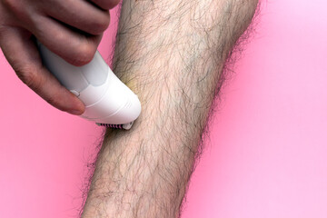 Man epilates his leg with an electric epilator device. close-up male leg shaver shaving. Skin Care...