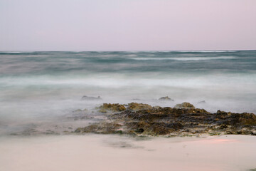 Long exposure shot of the ocean water and shore at sunset. Dreamy view of the blurred sea waves and rocks with magical twilight colors.