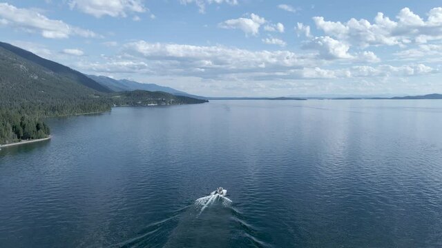 Lone Motorboat on Picturesque Calm Lake During Summertime on Flathead Lake in Kalispell, Montana - Aerial Drone Tracking View