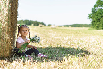 Naklejka na ściany i meble beautiful little girl with a bouquet of field daisies sat down to rest near a haystack on a summer day
